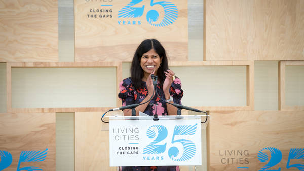 Lata Reddy smiles and applauds behind a podium at LC's 25th Anniversary.